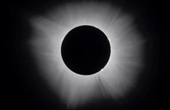 Total solar eclipse showing a dark lunar disc surrounded by a bright white corona against a black night sky