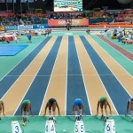Eight sprinters crouched in starting blocks on an indoor track, all waiting for the same starting signal