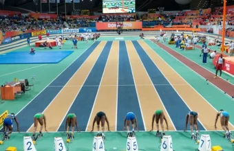 Eight sprinters crouched in starting blocks on an indoor track, all waiting for the same starting signal