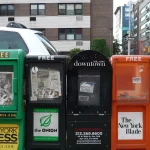 Rack of colorful newspaper vending boxes on a New York City sidewalk