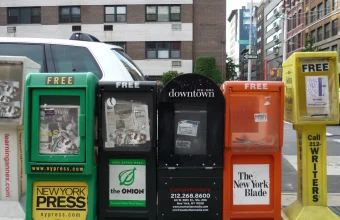 Rack of colorful newspaper vending boxes on a New York City sidewalk