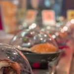 Colorful sushi plates under clear plastic domes queued along a conveyor belt sushi restaurant