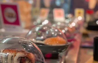 Colorful sushi plates under clear plastic domes queued along a conveyor belt sushi restaurant