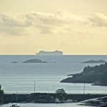 A cargo ship's silhouette distorted into an elongated shape by an atmospheric superior mirage above the horizon at sea