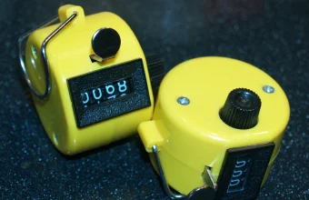 Two yellow mechanical tally counters resting on a dark speckled surface, one showing a four-digit count