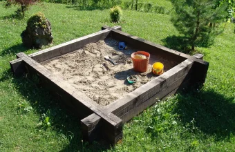 A real wooden outdoor sandbox filled with sand and toys, empty of people