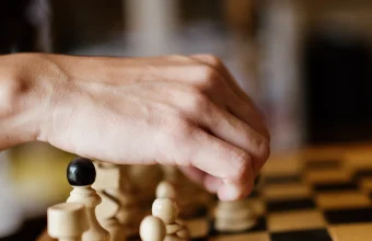 A hand reaches among a cluster of white chess pawns to move one piece on a wooden board, evoking a scheduler selecting which lower-priority workload to evict.