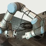 A Universal Robots UR16e collaborative robot arm with its controller and teach pendant resting on a workbench