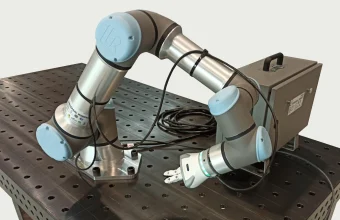 A Universal Robots UR16e collaborative robot arm with its controller and teach pendant resting on a workbench
