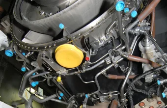 A dense wiring harness of tubes, hoses, and color-coded connector caps wrapped around a jet engine, with a technician working on the connections below
