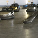 A row of bumper cars scattered freely across an indoor rink floor, contained by walls and a tire barrier