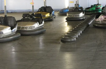 A row of bumper cars scattered freely across an indoor rink floor, contained by walls and a tire barrier