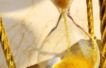 Golden sand flowing through the neck of a brass hourglass, pooling in the bottom bulb