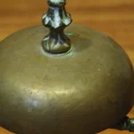 An ornate brass hotel concierge call bell on a wooden desk