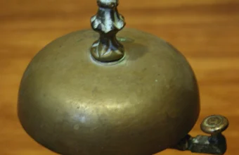 An ornate brass hotel concierge call bell on a wooden desk