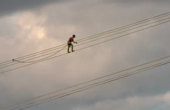A lineman walks along the conductor bundle of a high-voltage transmission line, performing maintenance directly on the live line carrying the load