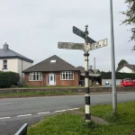 A weathered black and white cast-iron fingerpost with several arms pointing toward different destinations at a rural English road junction