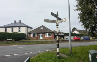 A weathered black and white cast-iron fingerpost with several arms pointing toward different destinations at a rural English road junction