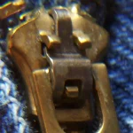 Macro photo of a zipper's slider mechanism engaging its teeth on a pair of denim jeans