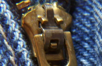 Macro photo of a zipper's slider mechanism engaging its teeth on a pair of denim jeans