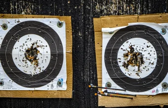 Two well-worn paper archery targets riddled with arrow holes, mounted on cardboard backing at an outdoor range