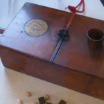 An antique 1814 wooden ballot box with voting balls and a small measuring cup on top, a literal visual metaphor for two-phase commit's voting phase