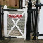 A small wicket gate built into a much larger railway level-crossing gate, providing a pedestrian path beside the main barrier