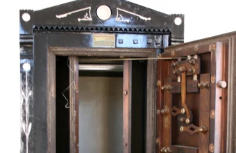 An antique bank vault door swung wide open, exposing its intricate mechanical locking bolts and the empty interior beyond