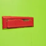 A red metal mail slot set into a bright green painted door
