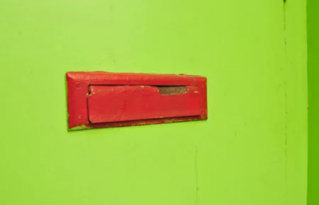 A red metal mail slot set into a bright green painted door