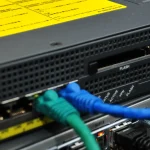 Close-up of the front panel of a Cisco ASA 5510 firewall mounted above a Cisco 1841 router, showing the Console, Aux, Reset, Flash and VPN labels with blue and green Ethernet patch cables