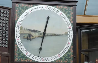 Painted auction clock with a black pointer sweeping a ring of numbers, beside a board of numbered buttons