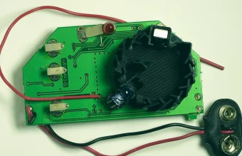 An open smoke sensor showing its green circuit board, black optical detection chamber and battery clip