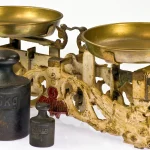 An antique two-pan balance scale with brass pans and iron weights, one marked 5 kg, on a white background