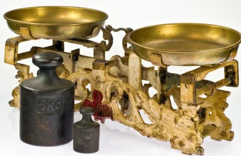 An antique two-pan balance scale with brass pans and iron weights, one marked 5 kg, on a white background