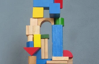 Colorful wooden toy blocks stacked into a tower with an arch, a tall blue pillar and a red triangle against a gray-blue wall