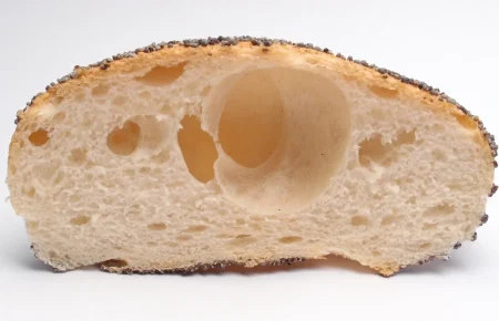 Cross section of a poppy seed bread roll with a large hole in the crumb
