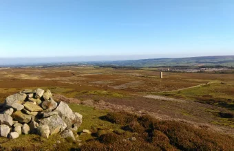 A pile of grey stones forming a cairn on open heather moorland under a clear blue sky