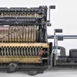 A Brunsviga 15 mechanical calculator with a crank handle, rows of number dials and a carriage, photographed against a white background
