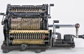 A Brunsviga 15 mechanical calculator with a crank handle, rows of number dials and a carriage, photographed against a white background