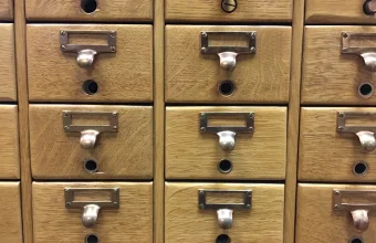 Rows of closed oak library card catalog drawers, each with a brass pull and a blank label holder