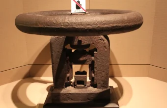 Cast-iron late Qing dynasty coin minting press with a large flywheel, displayed in a museum case