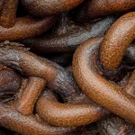 Close-up of heavily rusted iron chain links piled together, a visual for a weak link in a supply chain