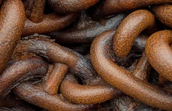 Close-up of heavily rusted iron chain links piled together, a visual for a weak link in a supply chain