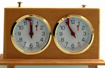 Wooden two-dial chess clock with brass-rimmed white faces showing different times