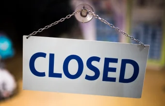 A white CLOSED sign with blue letters hanging from a suction cup and chain on a glass shop door