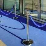 Blue velvet rope strung between chrome posts across the entrance of a glass storefront, a picture of an allow-list at the door