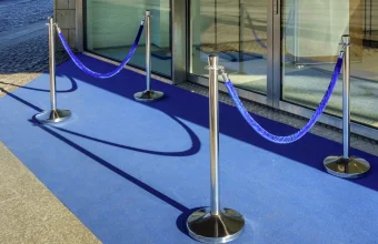 Blue velvet rope strung between chrome posts across the entrance of a glass storefront, a picture of an allow-list at the door