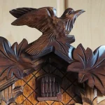 Carved wooden cuckoo bird perched above the leaf-carved roof and small door of a Black Forest cuckoo clock