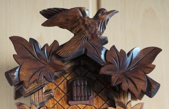 Carved wooden cuckoo bird perched above the leaf-carved roof and small door of a Black Forest cuckoo clock